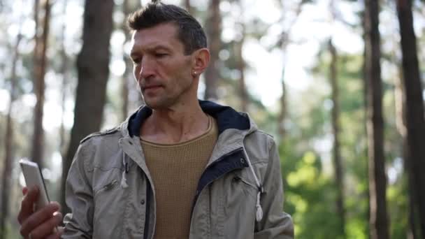 Anxious Caucasian man searching mobile network standing in sunny forest outdoors. Portrait of worried male tourist with smartphone in sunny spring summer woodland. Navigation and backpacking concept. — Video Stock
