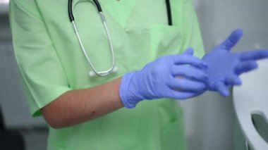 Hastanenin içinde tıbbi eldiven takan tanınmayan bir kadın. Genç beyaz doktor klinikte muayeneye hazırlanıyor. Sağlık ve uzmanlık kavramı.