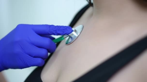 Close-up peito feminino com médico irreconhecível usando estetoscópio ouvir sons internos. Jovem mulher caucasiana submetida a exame médico na clínica dentro de casa. — Vídeo de Stock