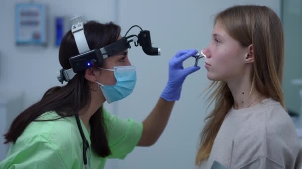 Side view focused Caucasian doctor checking nose of teenage patient in hospital indoors. Concentrated woman using nasal forceps checking nasal canal of teenage girl. Medicine and health concept. — Wideo stockowe