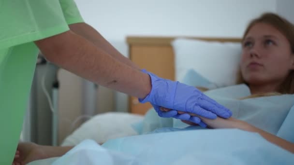 Unrecognizable female nurse holding hand of teenage patient and leaving hospital ward. Caring Caucasian young slim woman supporting endorsing ill girl lying in bed in medical clinic. — Stock Video