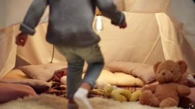 Comfortable tent in living room with toys and pretty little girl running inside in slow motion. Happy excited Caucasian kid enjoying leisure at home. Childhood and happiness.