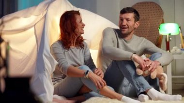 Wide shot happy adult couple hugging sitting at tent in living room talking in slow motion smiling. Loving Caucasian man and woman resting indoors at home on weekend. Romance and love. Slow motion.