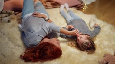 High angle view happy Caucasian mother stroking face of little daughter as girl touching woman nose. Smiling relaxed family resting in living room at home indoors. Lifestyle and love concept.