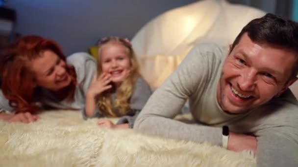 Porträtt av lycklig man skrattar tar selfie med dotter och fru liggande vid tält i vardagsrummet. Smartphone POV av avslappnad leende far make njuter fritid med familjen hemma på helgen. — Stockvideo