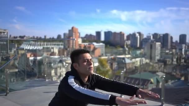 Concentrated Middle Eastern sportsman squatting on rooftop with beautiful urban city at background. Portrait of muscular confident young man working out on roof on Kyiv Ukraine. Lifestyle and sport. — Stockvideo