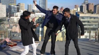 Şehirdeki güneşli bir günde çatıda dans eden üç rahat adam. Olumlu, kaygısız Orta Doğulu erkek arkadaşlar gün ışığında eğleniyor ve eğleniyorlar..