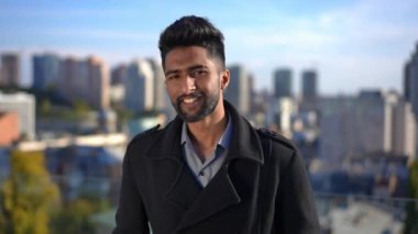 Genç, kendine güvenen, dişlek gülüşlü, dışarıda güneş ışığına poz veren kameraya bakan bir adam. Arka planda Kyiv Ukrayna ile gülümseyen Orta Doğulu yakışıklı adamın portresi.