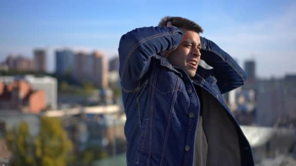 Stressed young man chocking freaking out standing on rooftop in urban city. Portrait of devastated Middle Eastern millennial guy looking at camera holding head in hands. Nervous breakdown concept. — Video