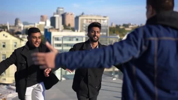 Joyful young men running to friend hugging mate standing on rooftop in sunshine. Smiling positive Middle Eastern friends greeting meeting in urban city outdoors on sunny day. — 비디오