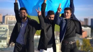 Ukrayna bayrağı taşıyan kendinden emin Orta Doğulu adamlar Kyiv Ukrayna 'nın çatısında duruyorlar. Şehir merkezinde güneşli bir günde poz veren genç ve yakışıklı arkadaşların portresi..