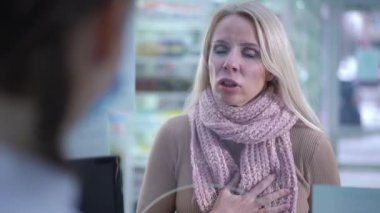 Upset beautiful woman complaining pain in chest standing at cashdesk in pharmacy. Portrait of sad Caucasian customer consulting druggist asking pharmacist for advice choosing pills.