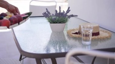 Tanınmayan beyaz kadın vitamin dolu tepsiyi cam masaya ağır çekimde koyuyor. Çiçekler cam hasır şapka ve terasta sağlıklı yiyecekler içiyorlar. Akşam yemeği ve öğle yemeği..