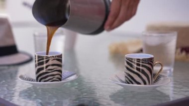 Pouring freshly brewed coffee in cups in slow motion. Unrecognizable Caucasian woman preparing romantic breakfast on summer terrace outdoors. Lifestyle concept.