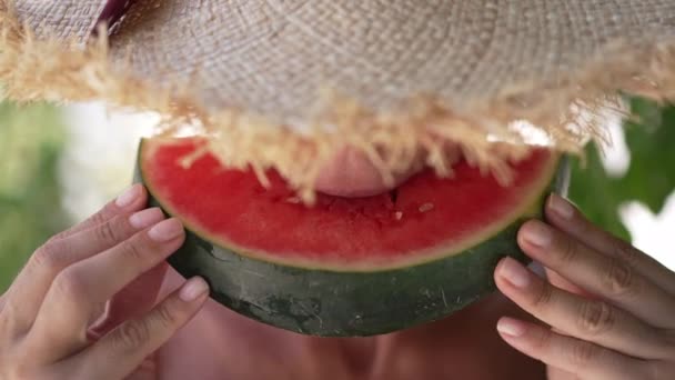 Primer plano mujer caucásica en sombrero de paja comer sabrosa sandía jugosa en cámara lenta. Vista frontal irreconocible relajado feliz mujer turista disfrutando de frutas tropicales sentado en la terraza al aire libre. — Vídeos de Stock