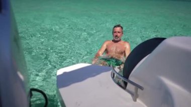 Akdeniz turkuazında yattan yavaş çekimde yüzen tatmin olmuş beyaz bir adam. Yetişkin erkek turist, Kıbrıs 'ta güneşli bir yaz gününün tadını çıkarıyor.