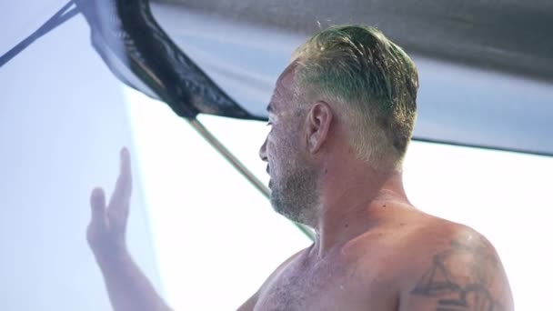 Close-up smiling positive boat captain waving looking away sailing in slow motion on sunny day outdoors. Happy relaxed Caucasian tattooed man driving yacht resting on summer vacations. — Stock video