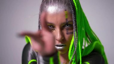 Yakından genç, zayıf bir kadın beyaz arka planda kameraya bakıyor. Kendine güveni tam, esnek jimnastikçinin portresi olağanüstü makyajlı, arkası eğilmiş eller..