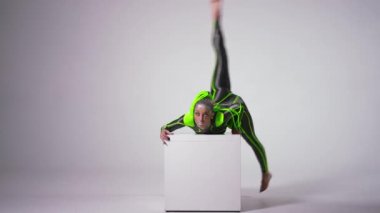 Wide shot portrait of confident beautiful artist rolling over cube at white background looking at camera. Young slim fit Caucasian woman performing posing indoors. Art and flexibility concept.