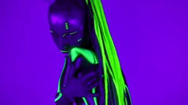 Parlak kostümlü floresan makyajlı kendine güvenen kadın portresi kameraya bakarak robot dansı yapıyor. Canlı kamera, hafif esnek dansçı olarak ultraviyole ışıkta poz vererek uzaklaşır..