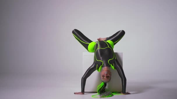 Brede shot flexibele turner met heldere make-up ondersteboven presteren op witte kubus op witte achtergrond. Portret van zelfverzekerde pasvorm Kaukasische jonge vrouw kijken naar camera dansen. — Stockvideo