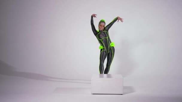 Wide shot portrait of confident gymnast in futuristic costume doing front walkover and looking at camera. Front view slim flexible Caucasian woman posing performing at white background. — Video