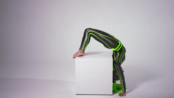 Side view slim young woman doing split in handstand at white background. Wide shot flexible Caucasian artist in futuristic costume performing. Modern art and impression concept. — стокове відео