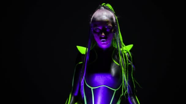 Front view futuristic woman with fluorescent makeup singing dancing bending at DJ set as live camera zoom out. Portrait of cyborg lady performing in neon light looking at camera posing. — Video