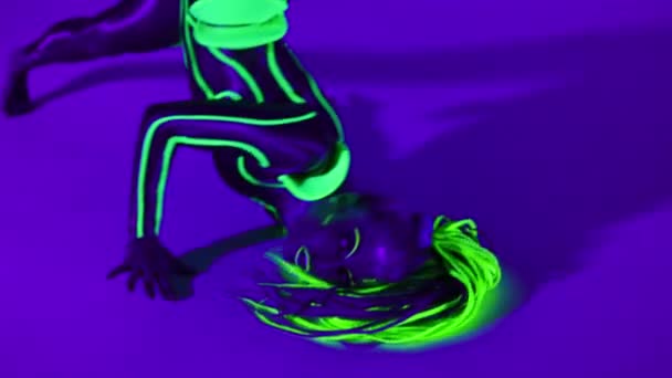 Young flexible performer posing bending in ultraviolet light looking at camera. Portrait of slim Caucasian woman with fluorescent makeup in costume dancing performing contemporary art. — Vídeos de Stock