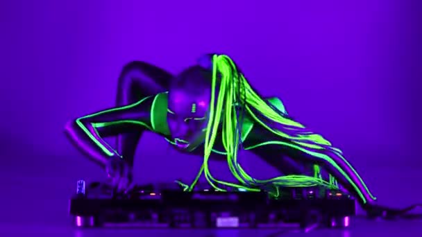 Geniş açılı cyborg kadın DJ 'in üzerinde dans ediyor ultraviyole ışıkta kameraya bakıyor. Modern sanatını sergileyen esnek, ince, beyaz floresan makyajlı, göz kamaştırıcı kostümlü bir sanatçı.. — Stok video