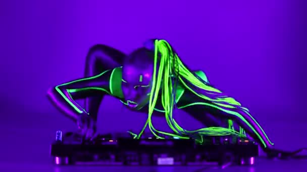 Wide shot cyborg woman dancing on DJ set in ultraviolet light looking at camera. Flexible slim Caucasian performer with fluorescent makeup in dazzling costume posing performing modern art. — Video Stock