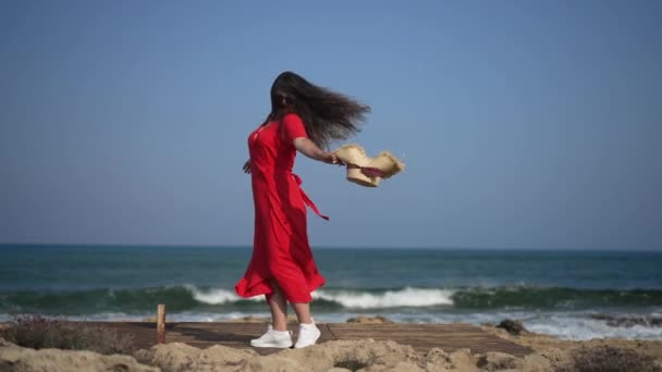 Excited happy woman in red dress spinning in slow motion enjoying summer vacations on Cyprus. Wide shot relaxed Caucasian tourist at background of Mediterranean sea. Tourism and happiness concept. — ストック動画