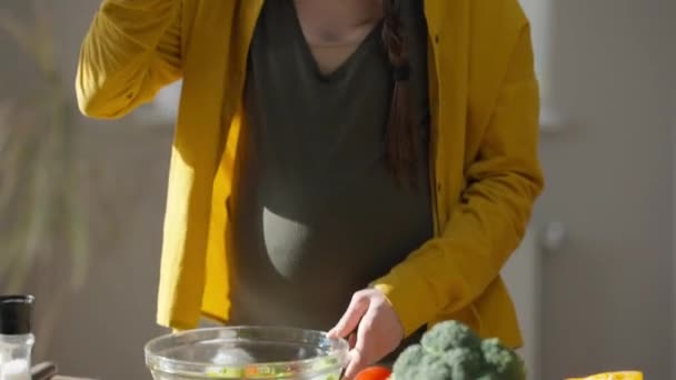 Pedestal shot of confident pregnant young woman tasting delicious vitamin salad indoors. Live camera moves up as slim attractive Caucasian expectant eating healthful food at home. Dieting pregnancy. – Stock-video