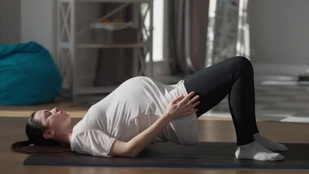 Side view concentrated pregnant sportswoman raising hips lying on exercise mat at home. Confident Caucasian beautiful woman training exercising indoors. — Stockvideo