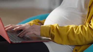 Hands of pregnant young woman typing on laptop keyboard indoors. Unrecognizable Caucasian relaxed expectant messaging online surfing Internet.