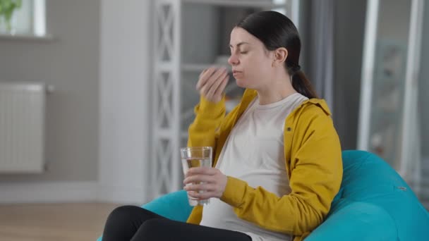 Side view pregnant woman taking in pills sitting on bag chair at home indoors. Portrait of Caucasian young expectant taking care of health. Pregnancy and medicine concept. — Videoclip de stoc