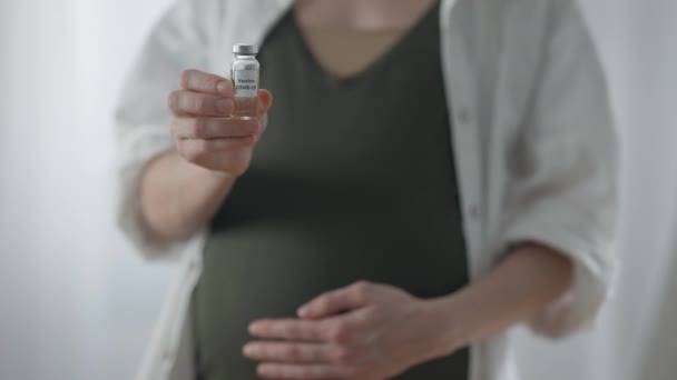Vacuna Covid-19 en la mano de una mujer embarazada borrosa irreconocible parada en el interior. Joven caucásica expectante publicidad coronavirus vacunación. Concepto de pandemia y embarazo. — Vídeo de stock