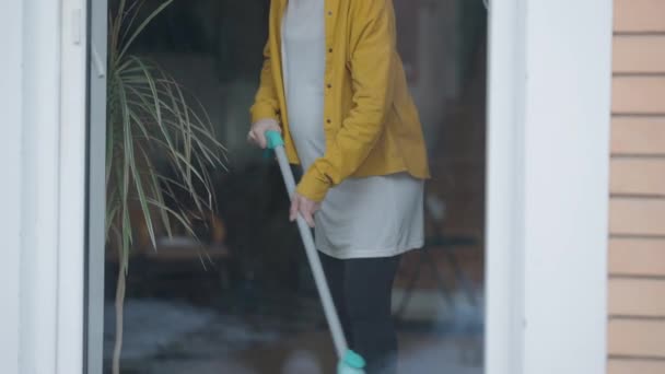 Young pregnant woman vacuuming floor at home having back ache sighing. Portrait of Caucasian expectant housewife indoors behind glass door. Live camera moves up. — Stok video