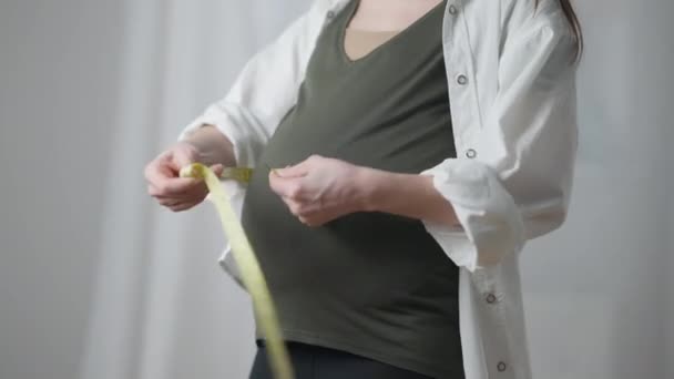 Unrecognizable pregnant woman measuring waist and belly standing indoors at home. Caucasian young slim expectant controls body weight and fetus. Health care and pregnancy. — Stok video