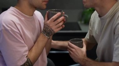 Tanımlanamayan beyaz eşcinsel çift kahve içerek evin içine burunlarını sürtüyor. Mutlu ve sevecen genç erkekler mutfaktaki sabahın tadını çıkarıyor..