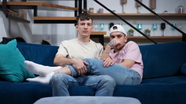 Ung homosexuell man lugnande ner pojkvän blev rädd titta på film i vardagsrummet hemma. Porträtt av kaukasiska HBTQ par njuter helgen fritid inomhus vilar på soffan. — Stockvideo