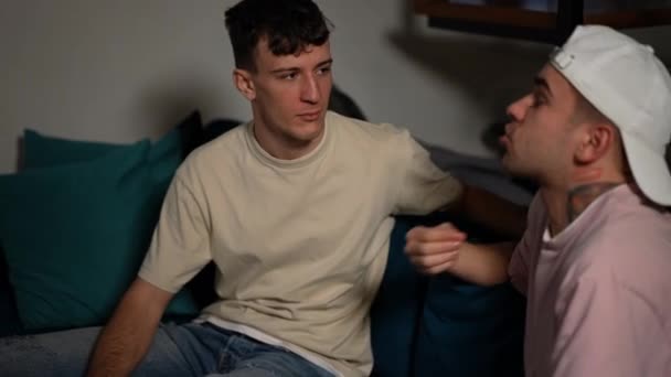 Портрет молодого кавказского гея, успокаивающего разъяренного партнера, кричащего сидя на диване в гостиной. Пара ЛГБТК ссорится дома. — стоковое видео