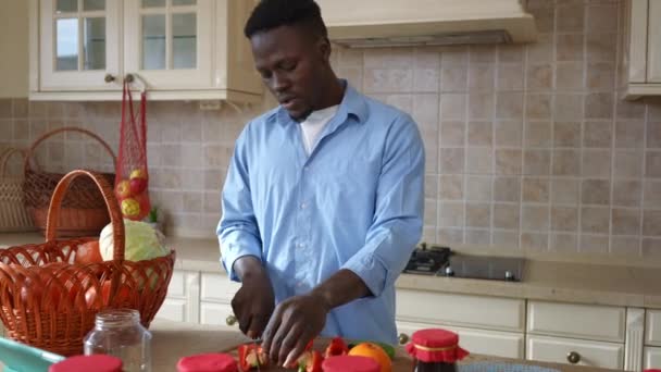 健康的な有機ビーガンサラダの歌のための自信を持って若い男切削成分のフロントビューの肖像画。アフリカ系アメリカ人の男料理でキッチンに自宅屋内. — ストック動画