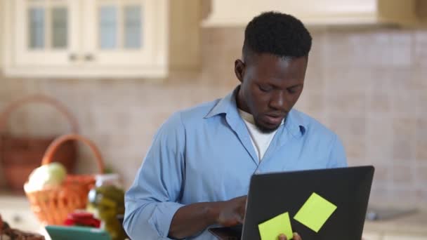 Pensativo hombre afroamericano concentrado navegar por Internet en el ordenador portátil en busca de recetas en línea. Retrato de un joven enfocado pensando en las frutas y verduras. — Vídeo de stock