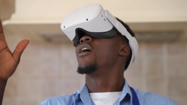 Primo piano vista frontale spensierato uomo afroamericano in VR cuffia da gioco online in piedi in cucina. Ritratto di giovane ragazzo felice e rilassato che si gode la realtà virtuale a casa dopo aver rotto la cottura. — Video Stock