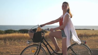 Bisikletli zayıf, genç, beyaz bir kadın. Alnına bakıp gülümsüyor. Akdeniz 'in sarı tarlasının arka planında gün ışığında kendine güvenen mutlu turist.