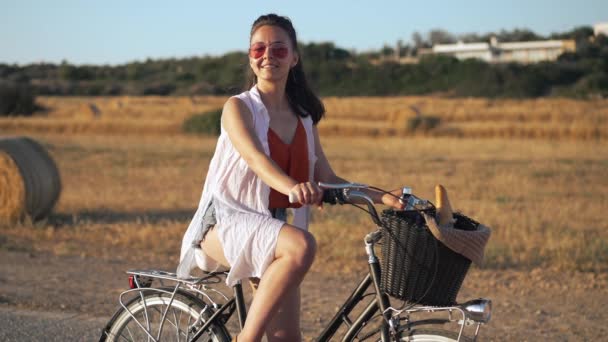 Glada leende kaukasiska ung kvinna vinka tittar på kameran poserar på bakgrunden av gula Cypern fält vid gyllene solnedgång. Porträtt av positiv vacker smal dam njuter sommar fritid utomhus. — Stockvideo