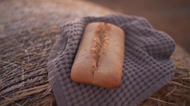 Primer plano sabroso pan de pan acostado en la toalla en la pila de trigo amarillo al aire libre. Deliciosa comida horneada en pajar de centeno en el campo rural. Concepto agrícola y agrícola. — Vídeo de stock