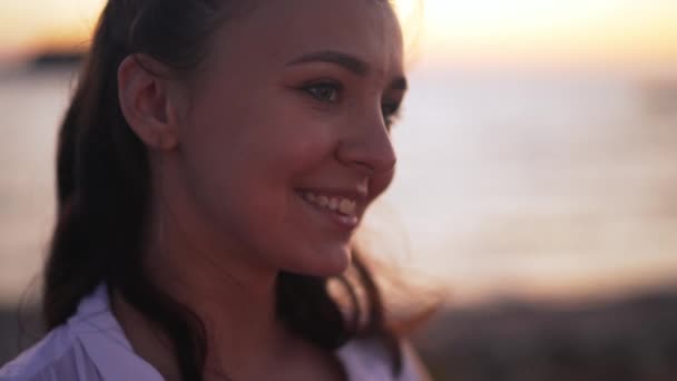 Hoofdfoto van een zelfverzekerde mooie glimlachende jonge vrouw die wegkijkt in het donker buiten op het strand. Gelukkig ontspannen Kaukasische toerist genieten zonsondergang schemering op Cyprus buiten. — Stockvideo