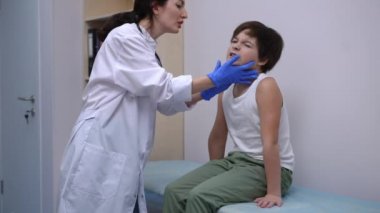 Hastanedeki muayene koltuğunda oturan üzgün, küçük beyaz çocuk boynunu kontrol ediyor. Tıbbi klinikte, otoların muayenehanesinde rutin kontrollere tabi tutulan sevimli bir çocuk.